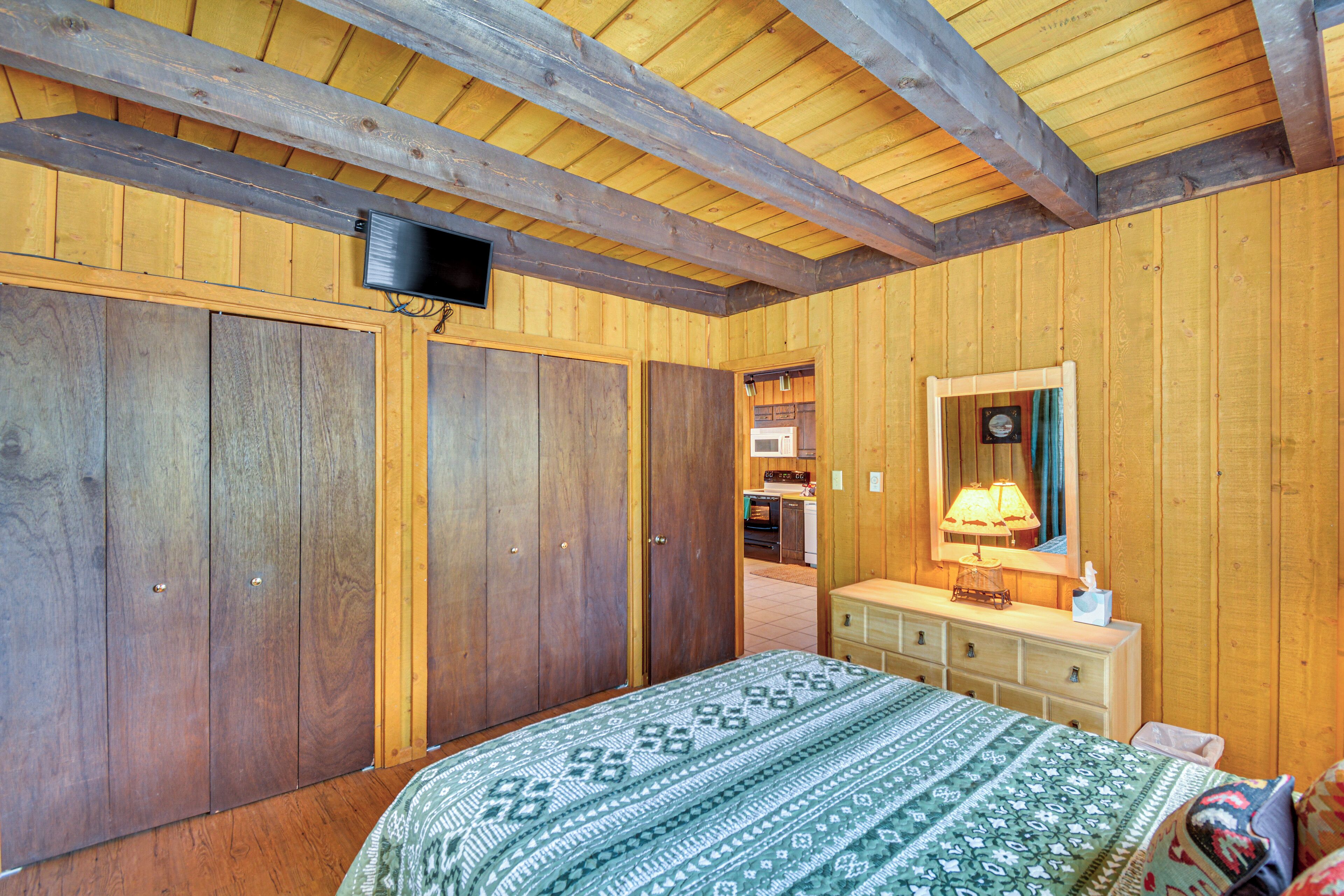 A wooden-paneled bedroom with a bed, dresser, and a television mounted on the wall.