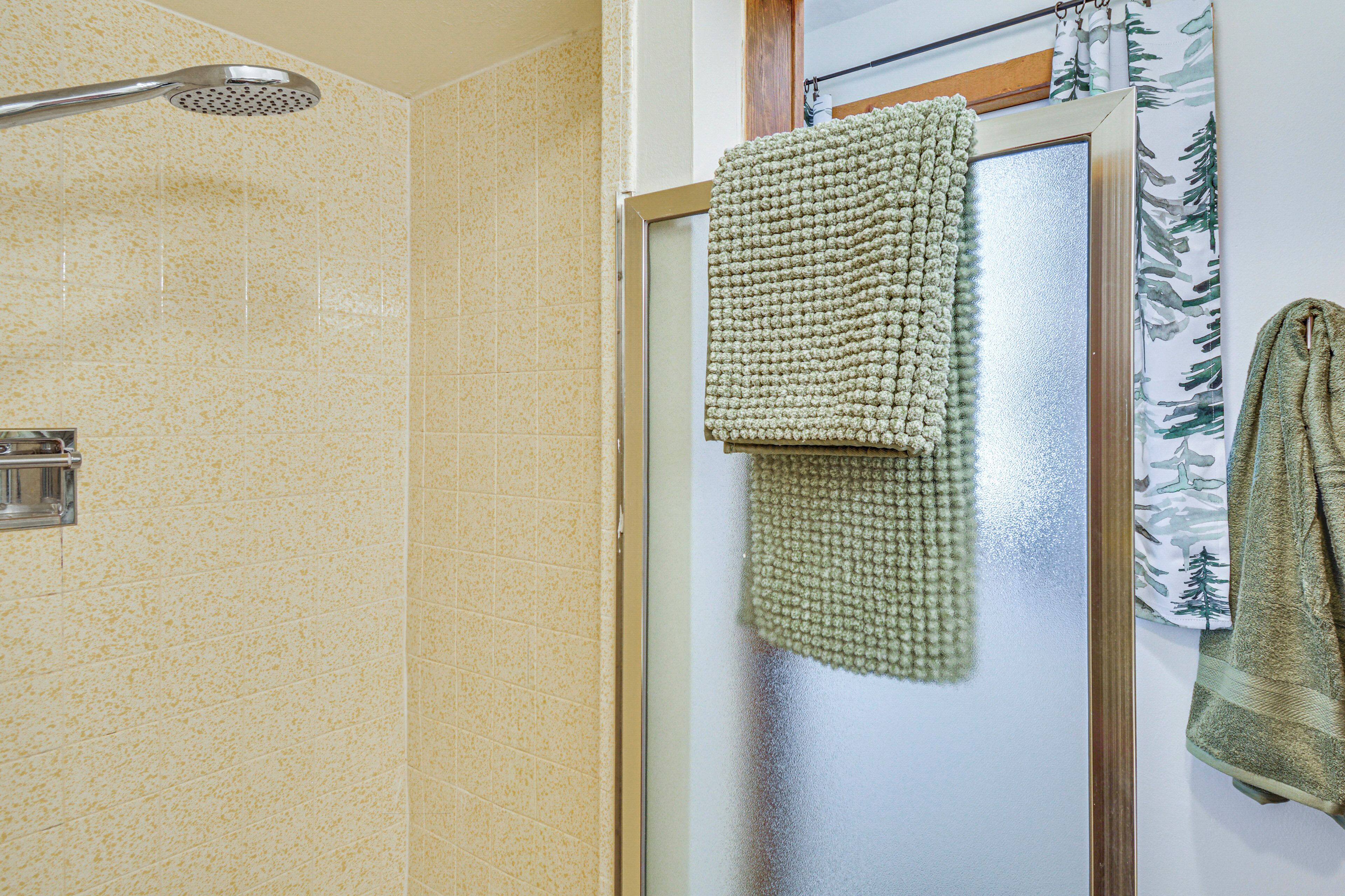 A bathroom with a shower, a towel rack with a green towel, and a glass door with a window.