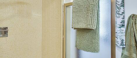 Un baño con ducha, un perchero y una toalla verde, y una puerta de cristal con ventanilla.