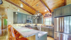 A spacious kitchen with wooden cabinets, a stainless steel refrigerator, and a central island with bar stools. - 4 Mi to Grandfather Mtn! Family-friendly Cabin (Newland)