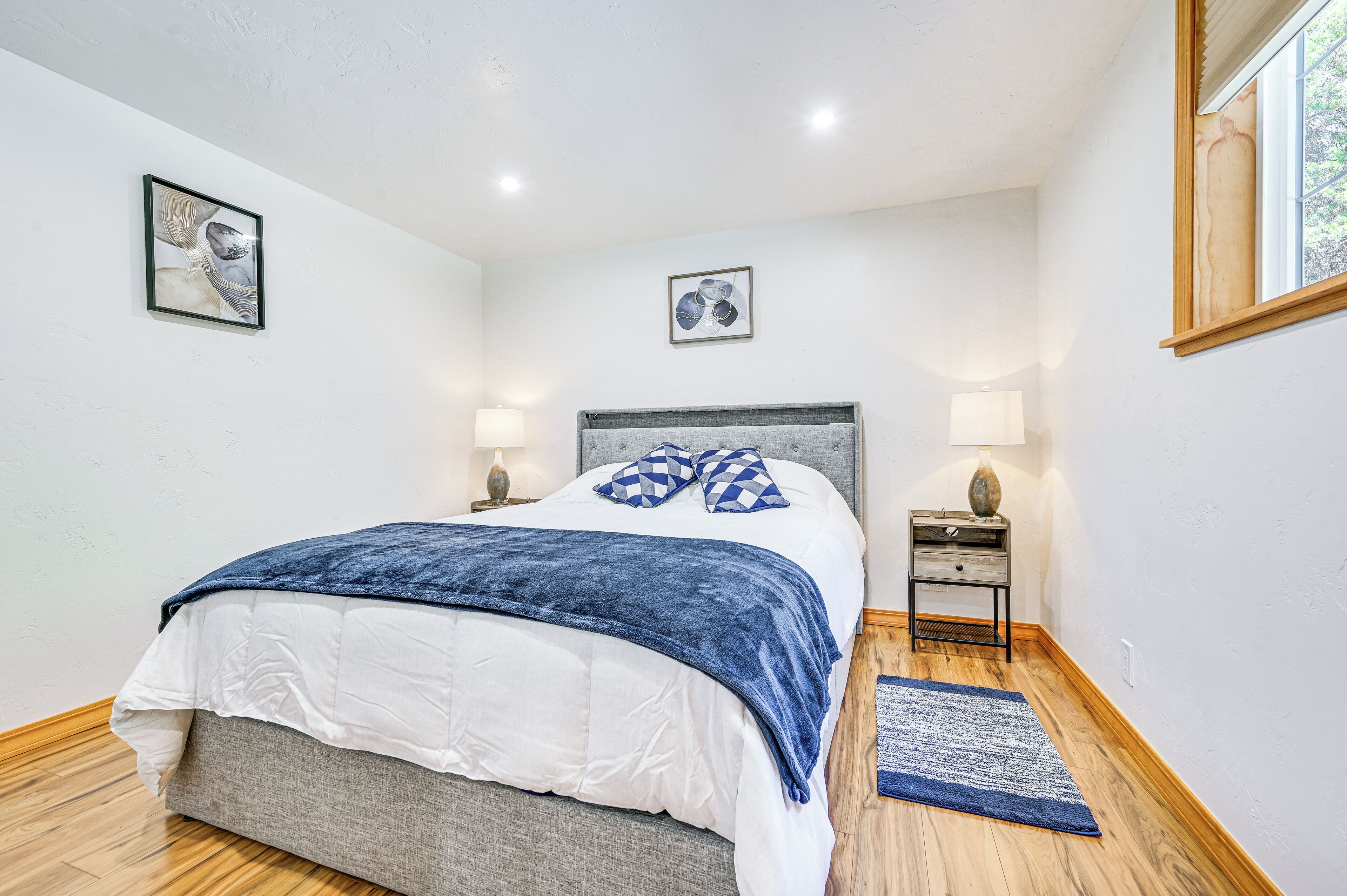 A bedroom with a bed, two bedside tables, a nightstand, a blue rug, and two wall-mounted lamps.