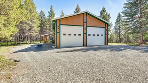A single-story building with a white garage door, surrounded by gravel, with a wooden exterior and green trim. - Peaceful Eureka Getaway - 1 Mi to Glen Lake! (Eureka)
