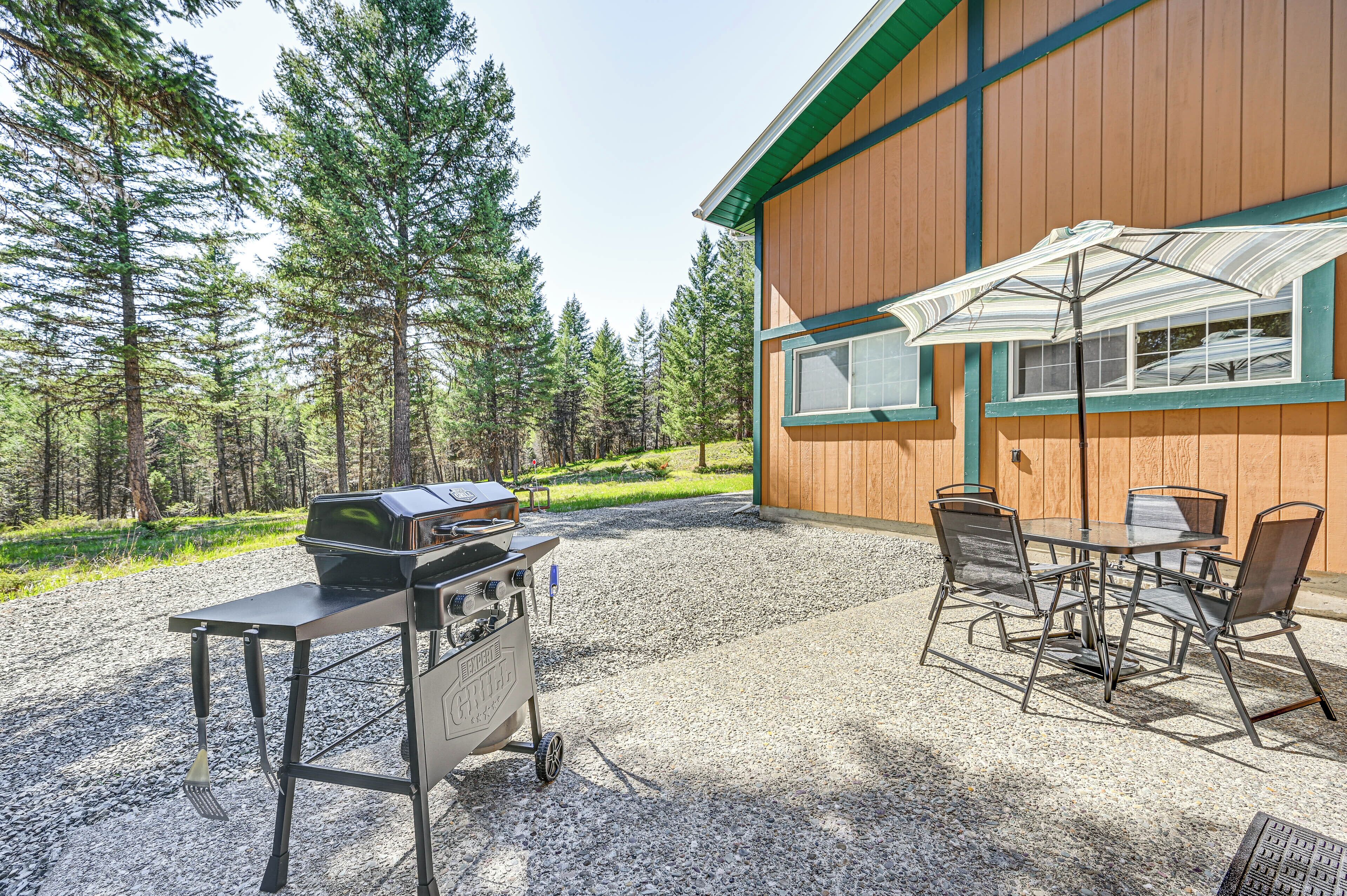 A gravel patio with a barbecue grill, a table with chairs, and an umbrella.