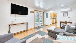 A modern living room with a flat-screen TV, a sofa, a coffee table, and a kitchen area in the background. - Peaceful Eureka Getaway - 1 Mi to Glen Lake! (Eureka)