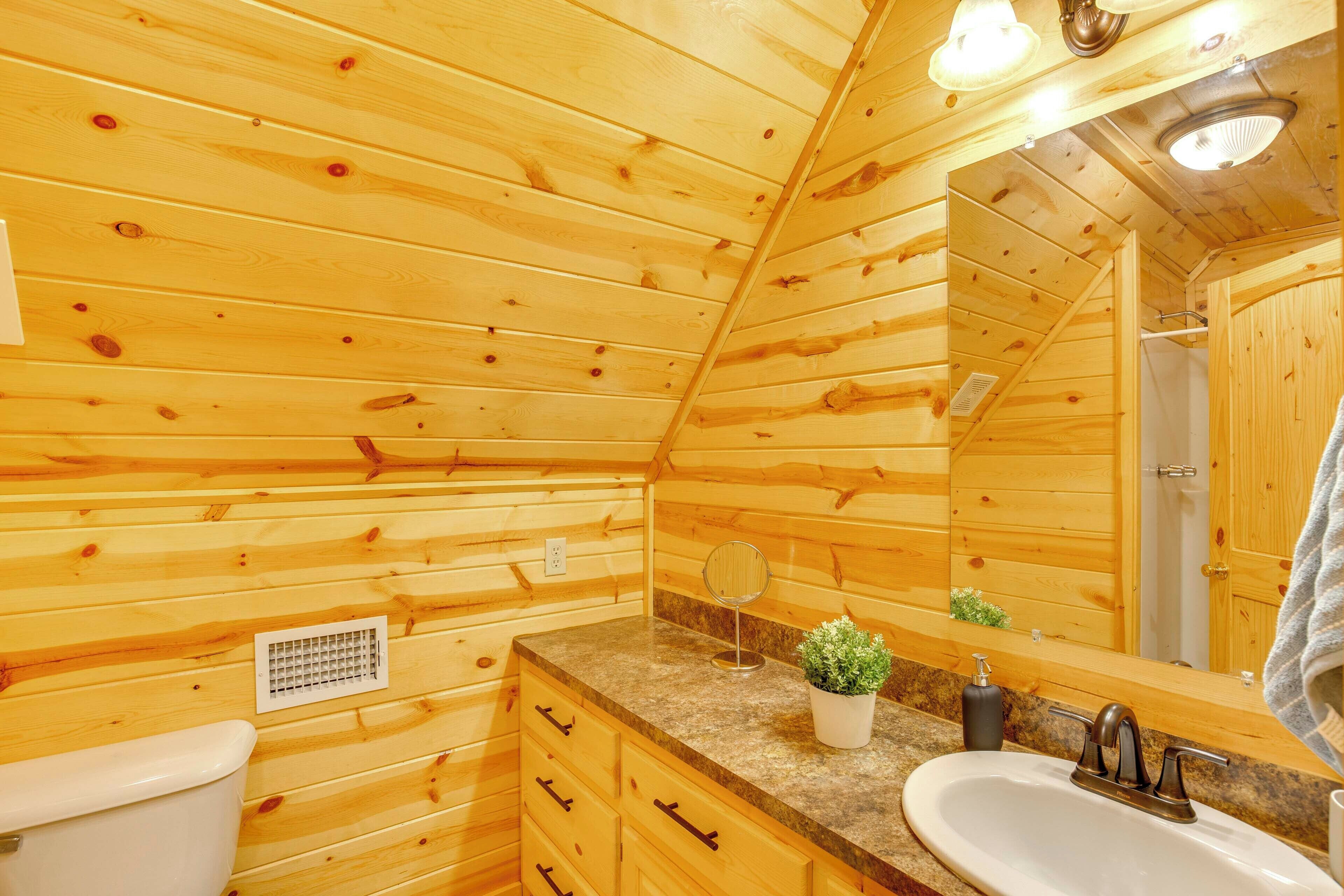 A wooden cabin bathroom with a sink, mirror, and toilet.