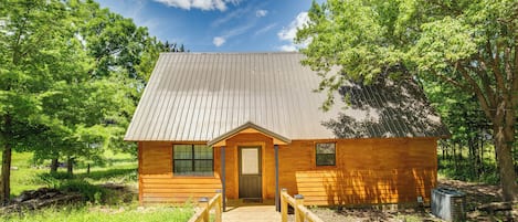 Eine Holzhütte mit einem Metall-Dach, einer Holztür und einem hölzernen Gang, der zu ihr führt.