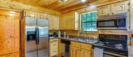 A modern kitchen with wooden cabinets, stainless steel appliances, and a stone tile floor.
