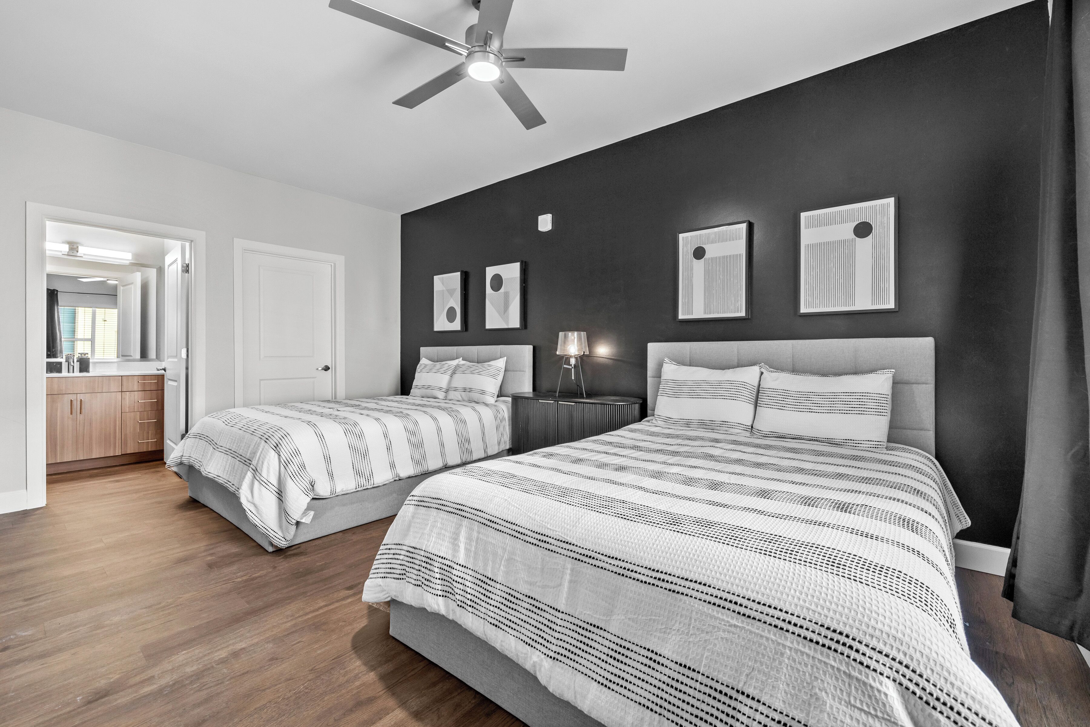 A bedroom with two beds, a ceiling fan, and a dark wall with framed pictures.