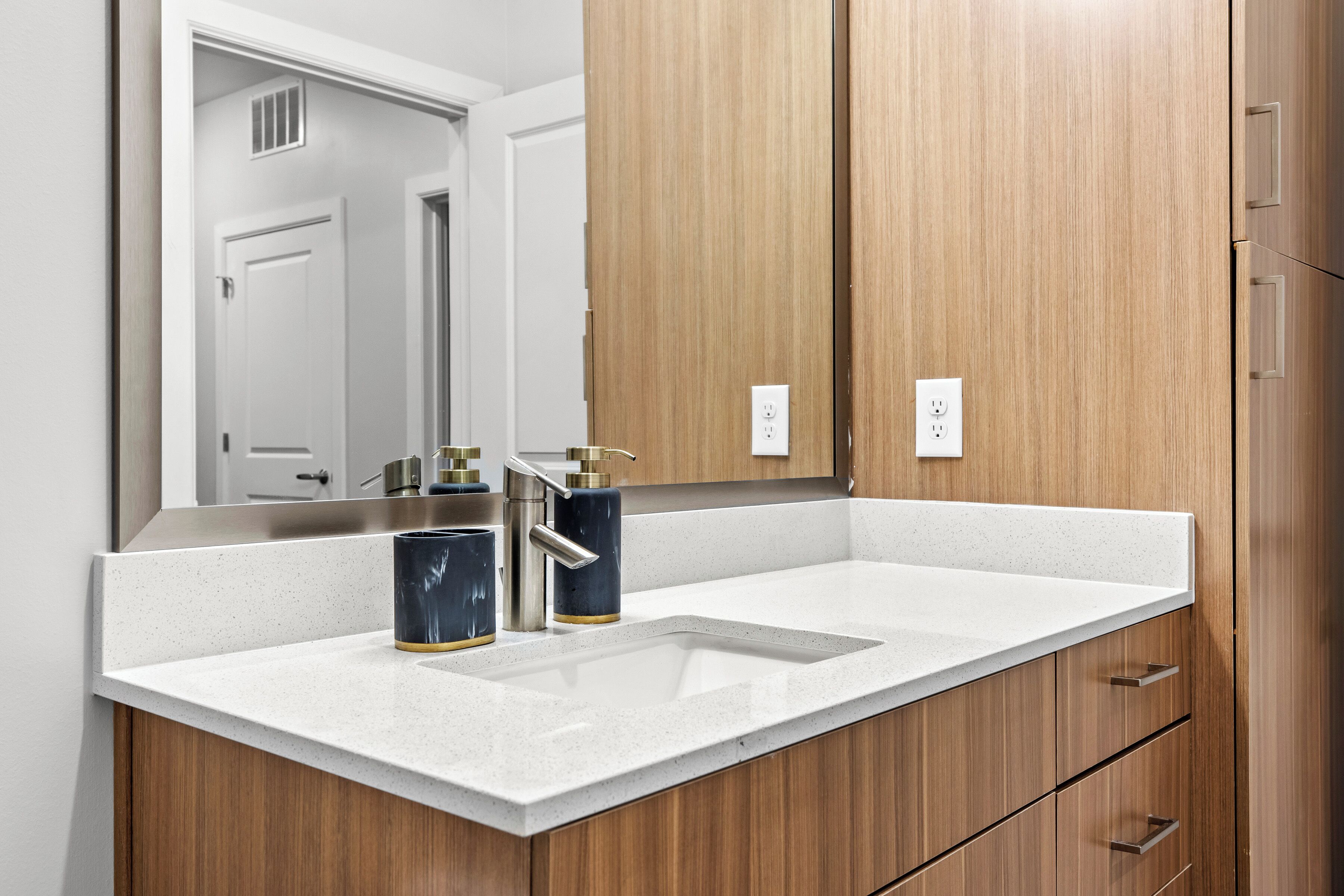 Un baño con encimera blanca, espejo y armarios de madera.