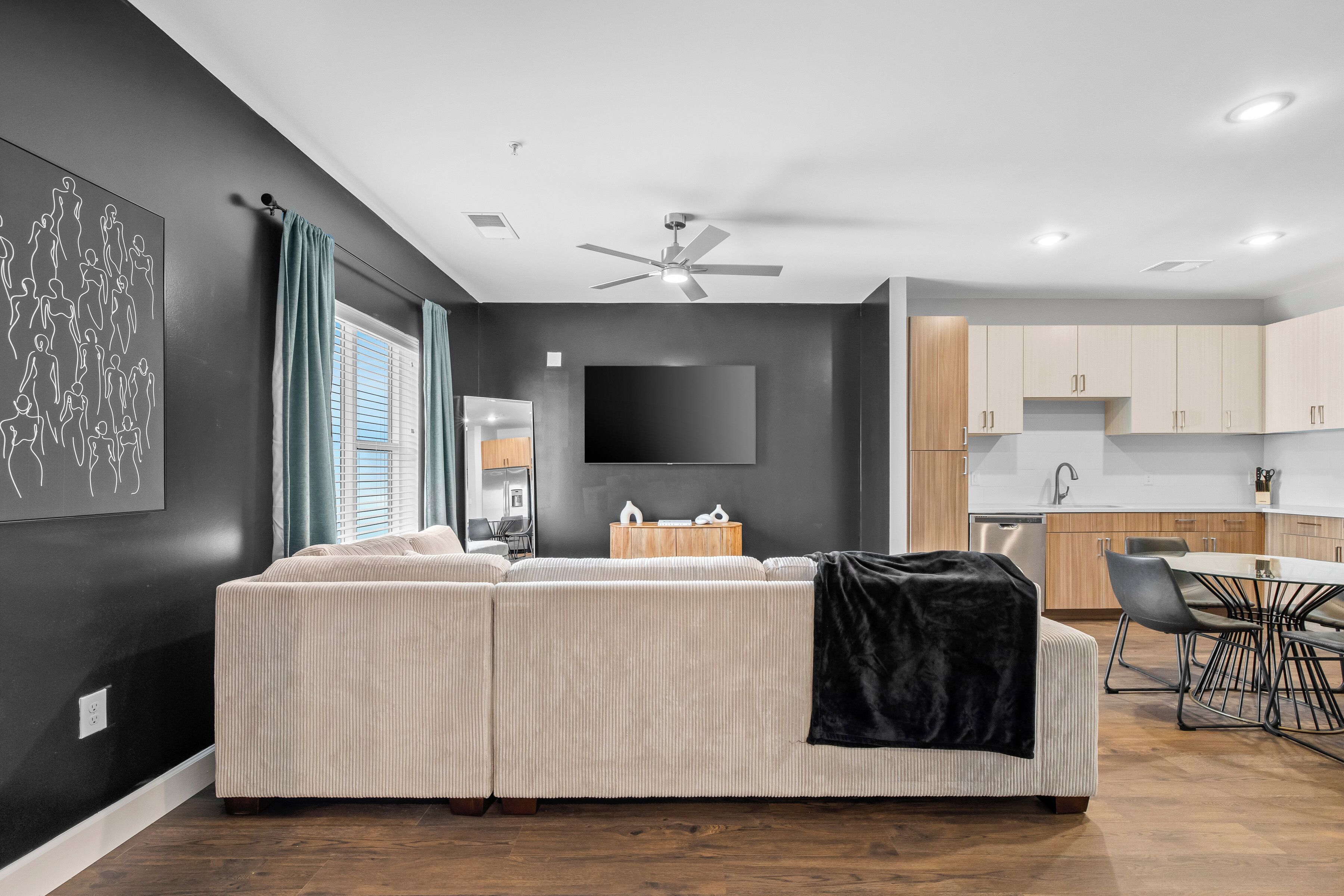 Een moderne woonkamer met een hoekbank, een flatscreen televisie en een eethoek met een tafel en stoelen.