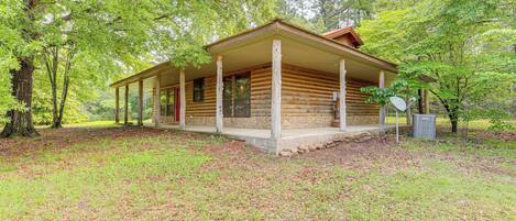 A log cabin with a porch, surrounded by trees and a grassy area.