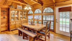 Un comedor de madera con una mesa grande, bancos y un aparador con puertas de vidrio.