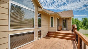 Une maison dotée d’une terrasse en bois, de grandes fenêtres et d’une porte donnant sur un porche abrité.