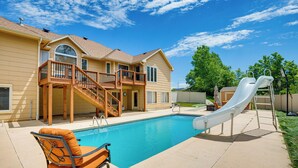 Un jardin à l’arrière d’une maison, avec une piscine, un toboggan et une terrasse.