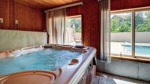 Un bain à remous avec un intérieur en bois, une fenêtre avec des rideaux et une vue sur un jardin avec une piscine.
