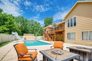 A backyard with a swimming pool, two orange chairs, a table with a decorative centerpiece, a wooden deck, and a white slide. - Junction City Home w/ Hot Tub - Near Milford Lake! (Junction City)