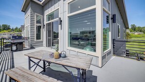 A modern house with large windows, a patio with a table and chairs, and a barbecue grill.
