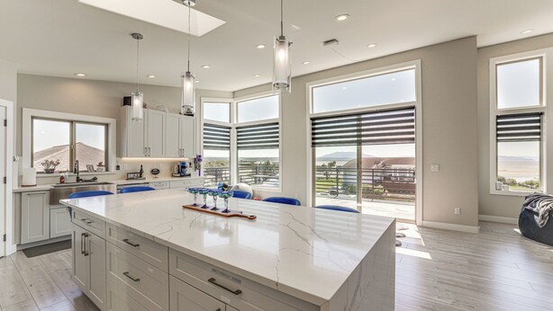 A modern kitchen with a large island, white cabinetry, and large windows offering a view of the outdoors.