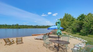 A beach with chairs, a table, and a blue umbrella.