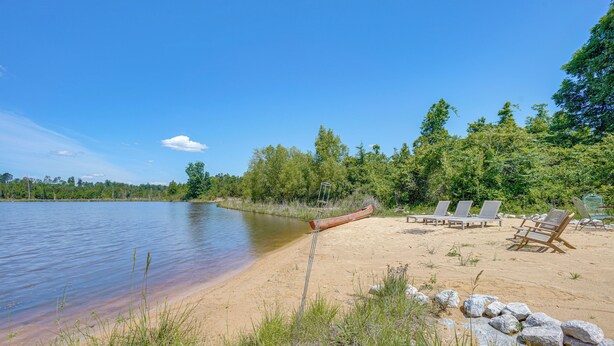 A lakeside beach with lounge chairs and a canoe.
