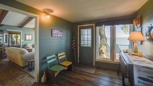 A cozy room with a bed, a bench, and a table with a lamp. There is a door leading to a balcony with a view of the ocean. - Dreamy Lake Poinsett Cabin w/ Deck, Dock & Views! (Arlington)