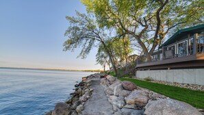 A waterfront walkway with a stone path, trees, and a building with a balcony overlooking the water. - Dreamy Lake Poinsett Cabin w/ Deck, Dock & Views! (Arlington)