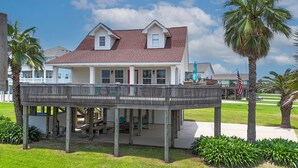 A two-story house with a wooden deck, a small porch, and a flag. - Gordeaux's Place: 3  BR, 2  BA House in Crystal Beach, Sleeps 8 (Bolivar Peninsula)