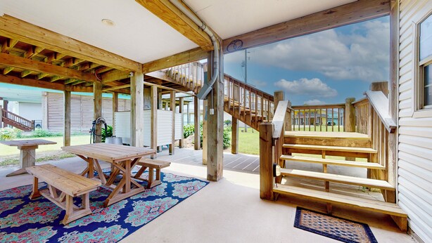 A covered outdoor area with a wooden table and benches, a staircase, and a view of the surrounding landscape. - Gordeaux's Place: 3  BR, 2  BA House in Crystal Beach, Sleeps 8 (Bolivar Peninsula)