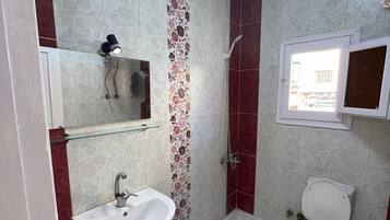 Un baño con lavabo, inodoro, ducha y un ventanal.