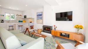 Een moderne woonkamer met een bank, een salontafel en een open haard. Er is een keuken met een eettafel en stoelen.