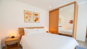 Een moderne hotelkamer met een groot bed, een houten hoofdbord, een nachtkastje met een lamp, en twee kunstwerken in lijsten aan de muur.