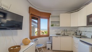 A compact kitchen with white cabinets, a built-in TV, a small dining area with a chair, and a view of the sea through an open window. - Villa Sierra Sea Views Quesada with private swimming pool (Ciudad Quesada)