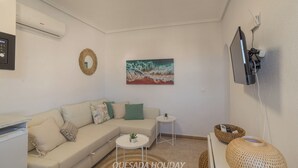 A living room with a sofa, a small side table, a painting, a TV mounted on the wall, and a wicker basket. - Villa Sierra Sea Views Quesada with private swimming pool (Ciudad Quesada)