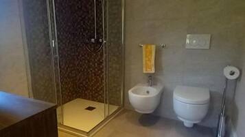 Un bagno con cabina doccia in vetro, un bidet, un water e un portasciugamani.