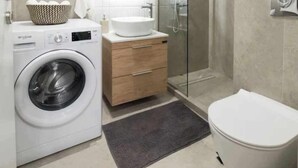 A modern bathroom with a washing machine, a sink, a toilet, and a glass shower enclosure. - Super luxury SUITE with Gym (Athina)