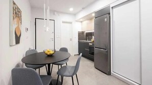 A modern kitchen with a stainless steel refrigerator, a dining area with a round table and chairs, and a white wall with a framed picture. - Super luxury SUITE with Gym (Athina)