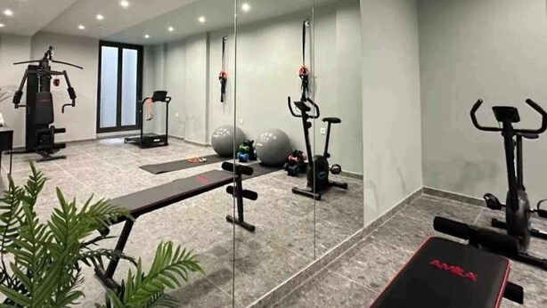A modern gym with exercise equipment, a mirrored wall, and a bench. - Super luxury SUITE with Gym (Athina)