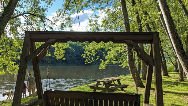Et legesæt i træ med gyngestol, et picnicbord og udsigt til en sø i en park.