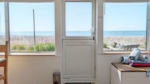 A room with a view of the beach, a wooden chair, a small table with towels, and a door.