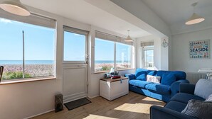 A spacious living room with a large window overlooking a beach, a blue sofa, and a white cabinet.