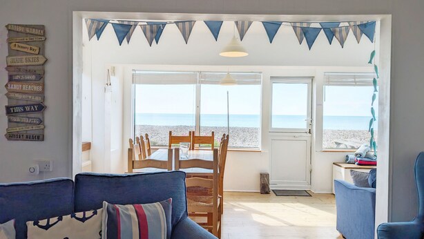 A living room with a view of the beach, a dining area with wooden chairs, and a blue sofa with striped pillows.