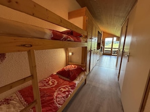 A bunk bed room with a wooden ceiling and a view of a green landscape through a door.