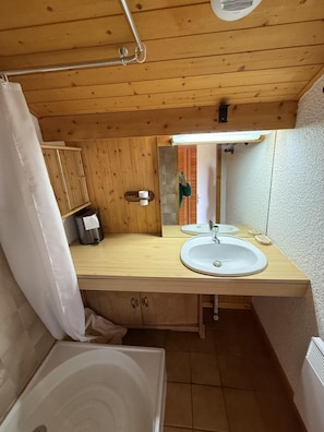 A compact bathroom with wooden paneling, a sink, a mirror, a shower curtain, and a toilet.
