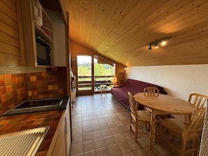 A compact kitchen with a dining area, wooden ceiling, and a view of the outdoors.