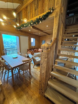 Cozy dining area with a wooden table and chairs, surrounded by a staircase and a large window offering a view of the town.