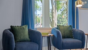 Dos sillones azules con cojines verdes, una mesita redonda y una lámpara colgante dorada.