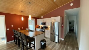 A modern kitchen with wooden ceiling, stainless steel appliances, and a central island with seating. - Yukon Hot Springs Villa #33 (Whitehorse)