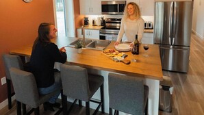A modern kitchen with wooden ceiling, stainless steel appliances, and a central island with seating. - Yukon Hot Springs Villa #33 (Whitehorse)