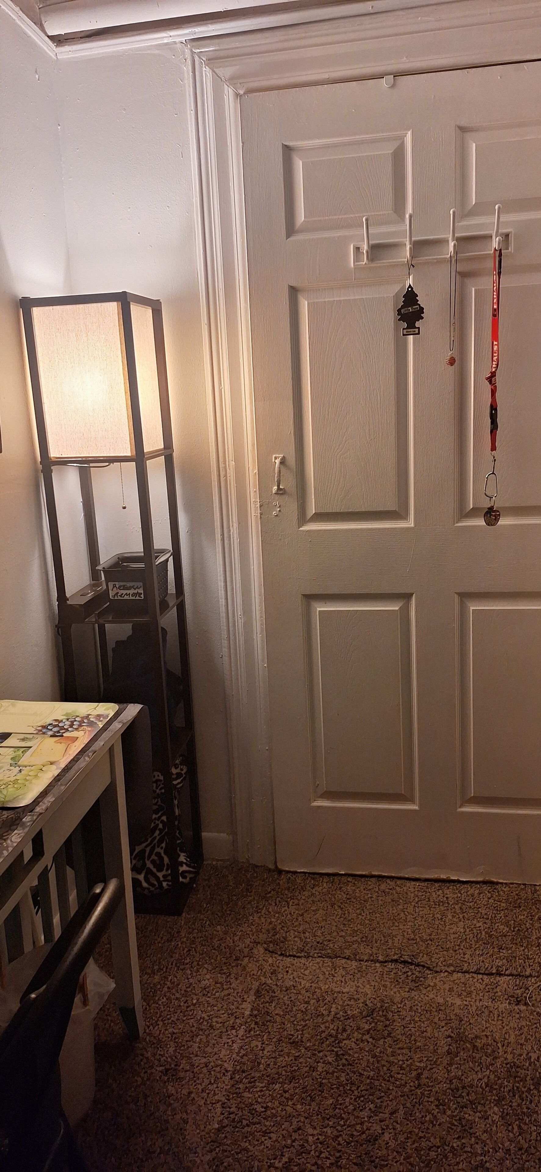 A room with a white door, a standing lamp, a table with a placemat, and a giraffe figurine on the floor.