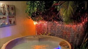 Ein Whirlpool mit Holzverkleidung, umgeben von Pflanzen und dekorativer Beleuchtung.
